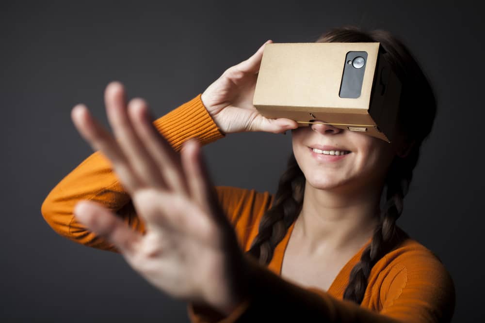 Color shot of a young woman looking through a cardboard, a device with which one can experience virtual reality on a mobile phone.