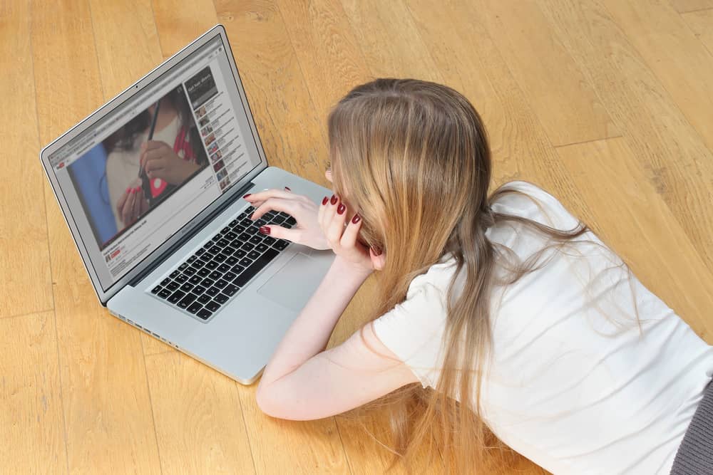 Teenage girl laying on the floor in front of laptop looking at YouTube videos searching for make up tutorials