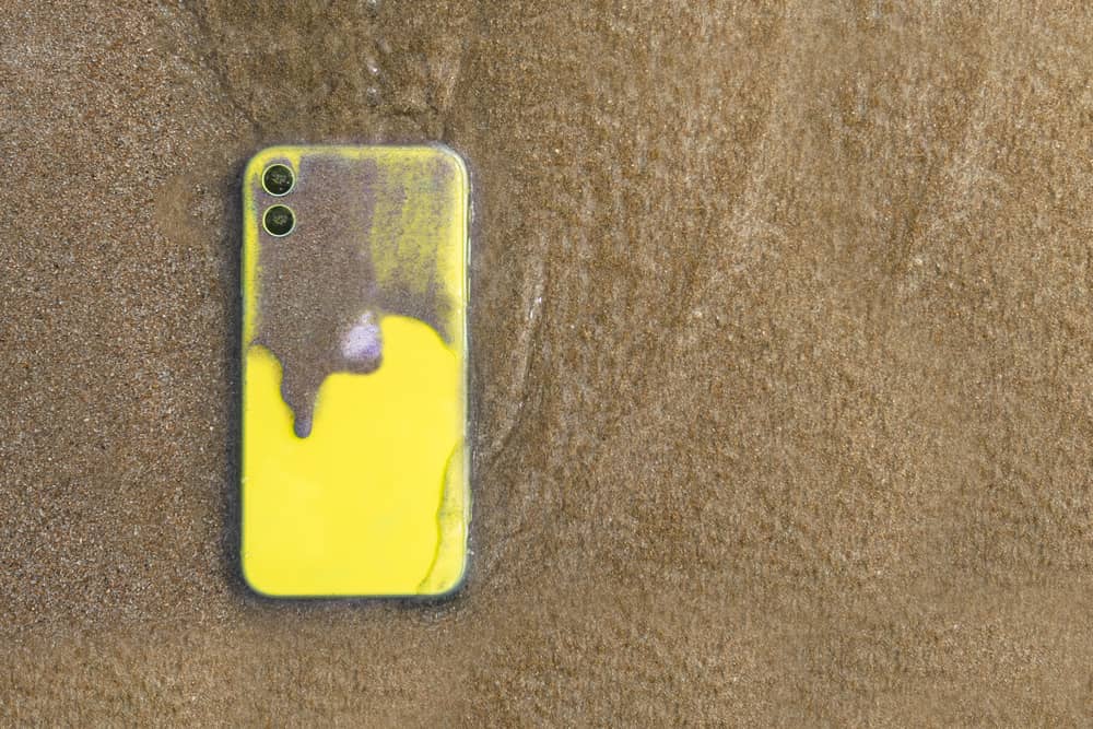 Yellow dirty iPhone 11 on sandy beach. 